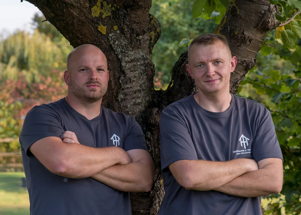 Marcell Hoffmann und Alexander Tramm in Firmenkleidung vor einem Baum